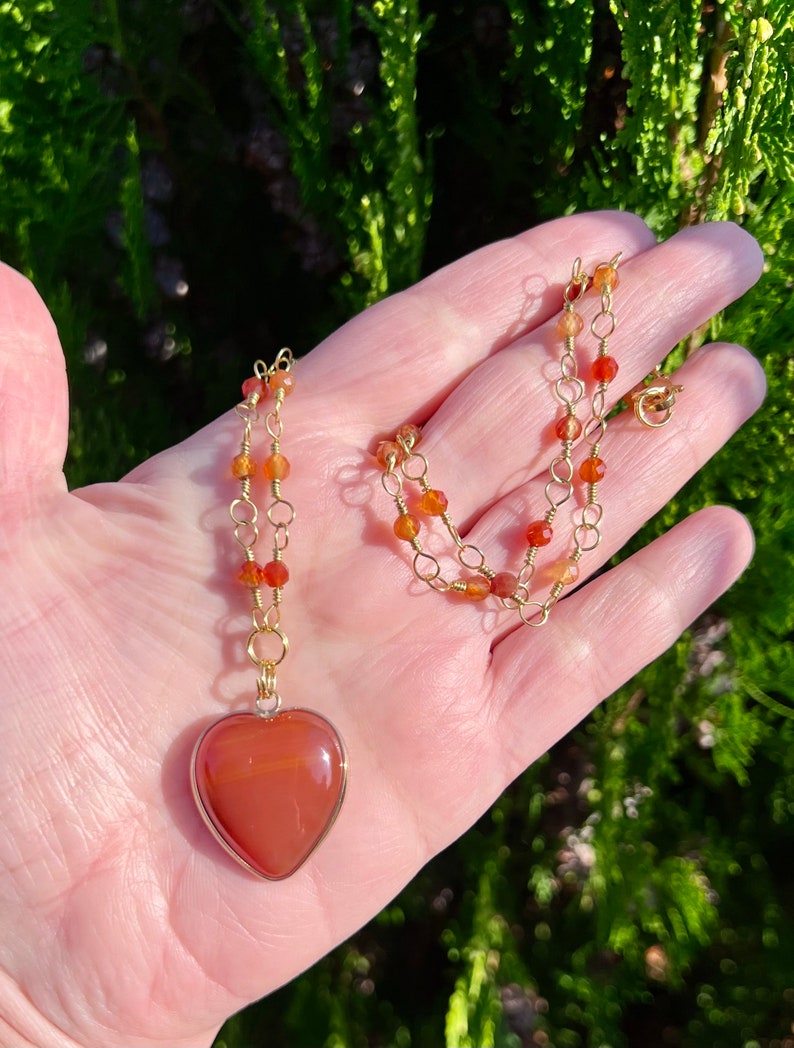 May include: A gold chain necklace with carnelian beads and a large carnelian heart pendant.