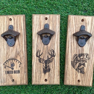 May include: Three wooden bottle openers with different designs. The first has a gas gauge with the text "I need beer". The second has a deer head. The third has a bass fish.