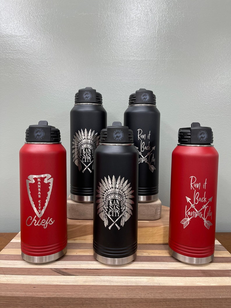 May include: Five stainless steel water bottles with different designs. The bottles are red and black with silver lids. The designs include a Native American headdress, an arrow, and the words "Run it Back Kansas City".