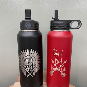 May include: Two stainless steel water bottles with lids and handles. The black bottle has a Native American headdress design with the text "Kansas City". The red bottle has the text "Run it Back Kansas City" with two crossed arrows.