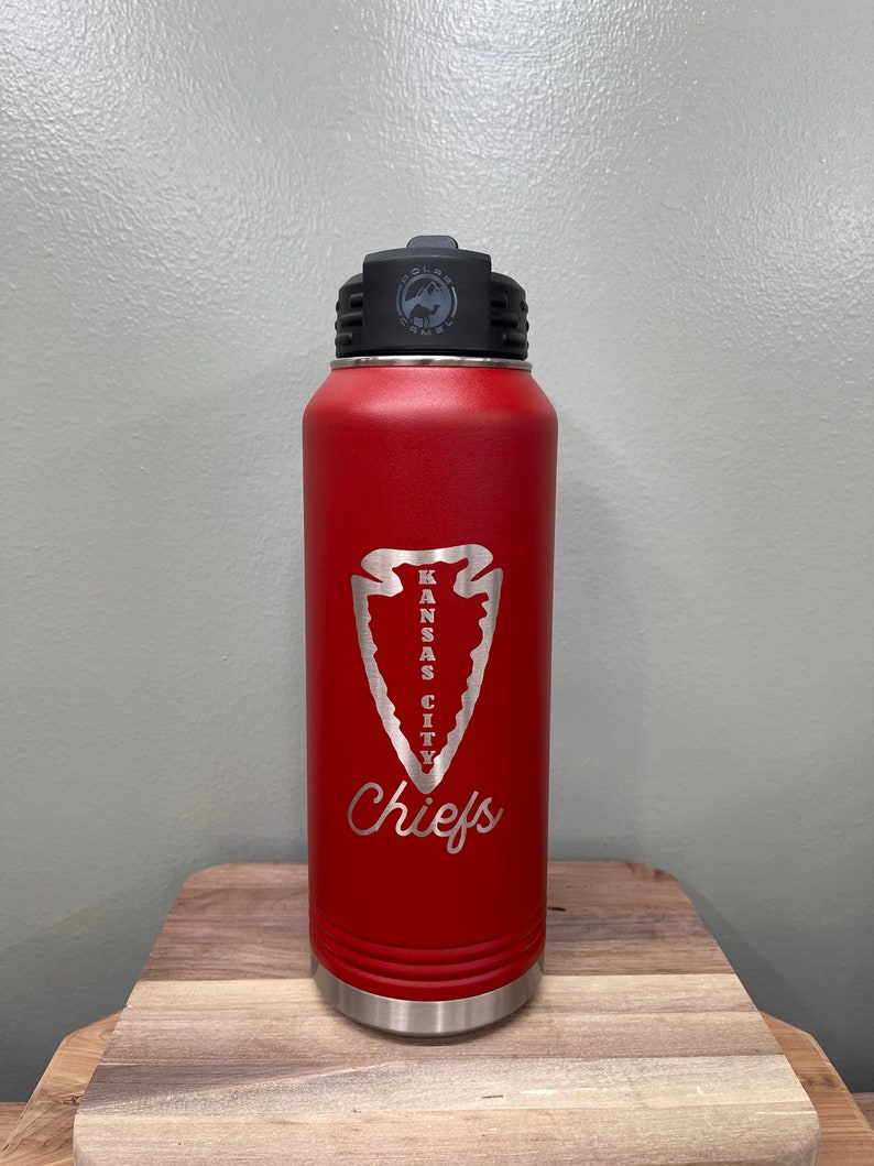 May include: Red stainless steel water bottle with a black lid and a silver inscription that reads "Kansas City Chiefs" with an arrowhead design.