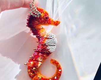 Puede incluir: Broche de caballito de mar hecho a mano, con un vibrante degradado de lentejuelas naranjas, rojas y blancas. El caballito de mar tiene una corona y un ojo enjoyados, con detalles dorados y de cristal. Un accesorio único y llamativo.