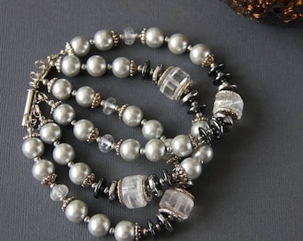 May include: A triple strand necklace with silver and gray beads. The necklace features clear faceted crystal beads and black hematite beads.