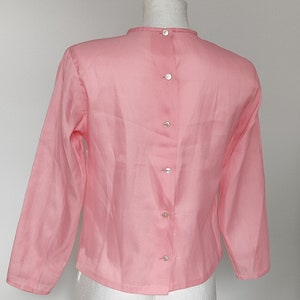 Op de afbeelding: Een roze blouse met lange mouwen en een knoopsluiting op de rug.