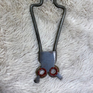 May include: A vintage metal tool with a pointed tip, a handle with a lever, and two red rings at the bottom. The tool is designed for a specific purpose, possibly for crafting or repair.
