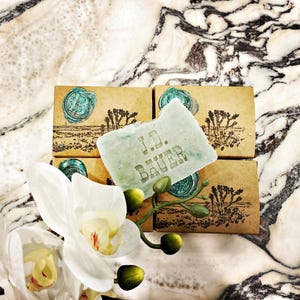 May include: Four small boxes with a green bar of soap on top. The soap has the words "J.D. BAUER" embossed on it. The boxes are brown with a design of a desert landscape and a wax seal.