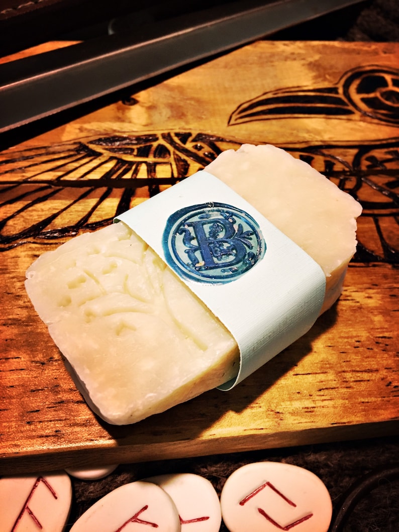 May include: A bar of white soap with a decorative design wrapped in a light blue paper with a wax seal featuring the letter "B".