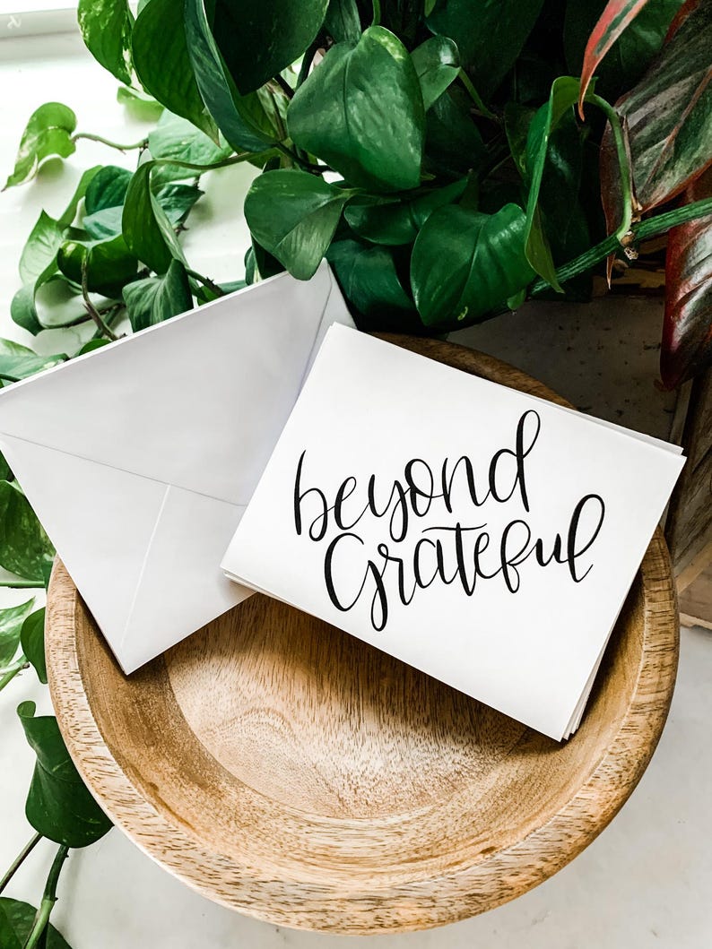 May include: A white card with black calligraphy that reads "beyond grateful" on a wooden surface.