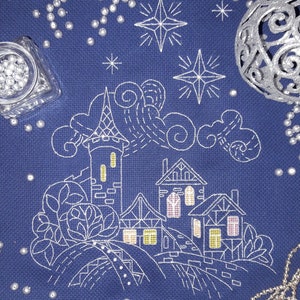 Könnte beinhalten: Weiße Stickerei auf einem dunkelblauen Stoff, die ein kleines Dorf mit einem hohen Turm, Bäumen und Wolken unter einem sternenklaren Nachthimmel darstellt.