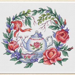 May include: A blue and white teapot with a floral design sits in a wreath of green leaves and red roses. A matching teacup and saucer are in front of the teapot.