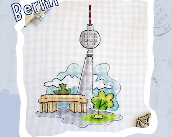 May include: A cross-stitch design featuring the Berlin TV Tower, a bench, and two trees. The tower is gray with a red and white antenna. The bench is brown and the trees are green. The background is a light blue watercolor wash.