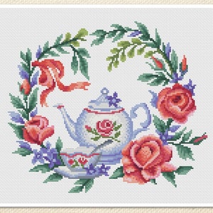 May include: Cross-stitch design of a teapot and teacup encircled by a floral wreath. The teapot is pale blue with a rose motif, and the wreath includes red roses, purple flowers, and green leaves. A red ribbon is tied at the top of the wreath.