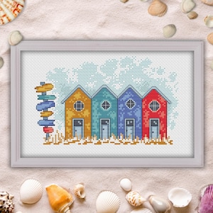 May include: Cross-stitch pattern of four colourful beach houses with a signpost in front. The houses are yellow, blue, purple, and red. The background is a light blue sky with white clouds.