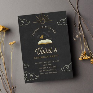Op de afbeelding: Een zwarte uitnodigingskaart met gouden letters voor een verjaardagsfeest. De kaart toont een boek met een zon en wolken op de achtergrond. De tekst luidt: "Kom gezellig mee naar Voilets verjaardagsfeest. Zondag 19 februari 15:00-20:00 uur Diner & drankjes 123 Basgiath St. RSVP 555-555-5555"
