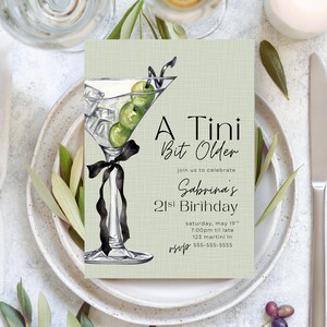 May include: A rectangular invitation card with a light green textured background featuring a watercolor illustration of a martini glass with three green olives and a black ribbon. The text reads A Tini Bit Older, join us to celebrate Sabrina's 21st Birihday, saturday, may 19th, 7:00pm til late, 123 martini ln, rsvp 555-555-5555.