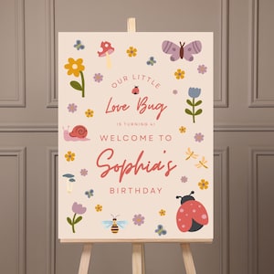 May include: A welcome sign for Sophia's birthday, featuring a light beige background with colorful illustrations of flowers, insects, and the text "Our Little Love Bug is turning at Welcome to Sophia's Birthday."