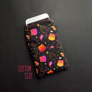 May include: Black phone sleeve with a Halloween-themed pattern. The fabric features colorful cartoon ghosts, cats, and the word "BOO!" in speech bubbles. The text "CUSTOM SIZE" is printed in pink.