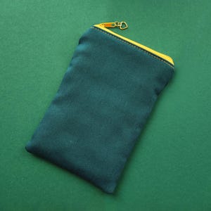 Pu&ograve; includere: Un astuccio in tela verde acqua con cerniera e finiture gialle. L'astuccio rettangolare &egrave; chiuso con una cerniera dorata e poggia su una superficie verde. Design semplice e minimalista.