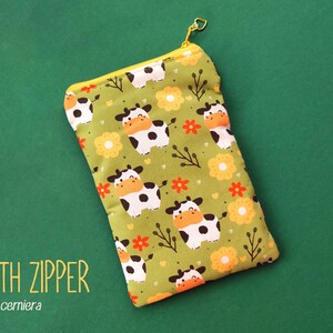 Pu&ograve; includere: Un astuccio rettangolare in tessuto verde con cerniera gialla e tiretto dorato. L'astuccio &egrave; decorato con mucche dei cartoni animati, fiori arancioni e ramoscelli. Il testo "WITH ZIPPER" &egrave; stampato in basso a sinistra.