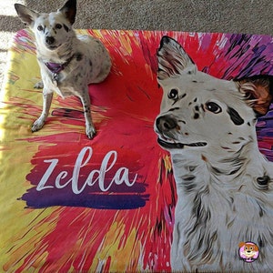 Op de afbeelding: Een kleurrijk hondenkleed met een witte hond met zwarte vlekken. De naam van de hond, Zelda, staat in wit op het kleed.