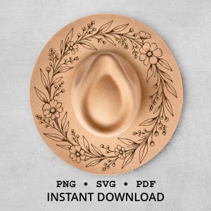 Puede incluir: Sombrero fedora beige con un diseño floral alrededor del ala. El sombrero tiene una copa redondeada y un ala ancha. El diseño floral es de color marrón oscuro. El texto "PNG • SVG • PDF DESCARGA INSTANTÁNEA" está en la parte inferior.