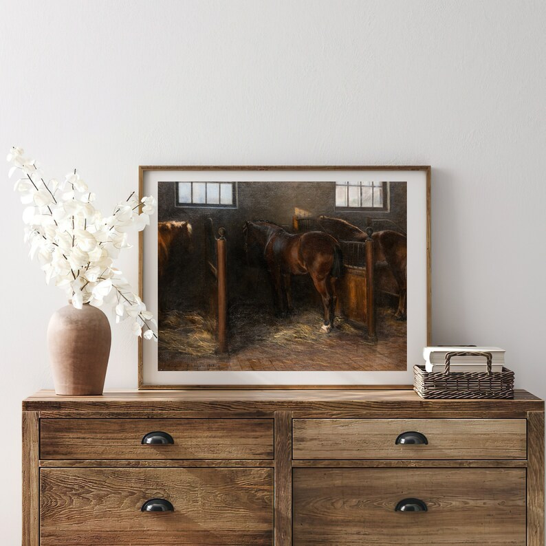 Peut inclure: Une peinture encadr&eacute;e repr&eacute;sentant une &eacute;curie avec trois chevaux bruns debout dans leurs stalles. Les chevaux sont tourn&eacute;s dos au spectateur, et les stalles sont en bois. La peinture est plac&eacute;e contre un mur blanc avec un vase de fleurs blanches sur une commode en bois.