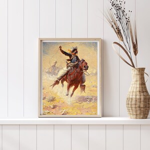 Op de afbeelding: Een vintage schilderij van een cowboy die een bruin paard berijdt en een stier lassoeert in een stoffig, geel landschap. De cowboy draagt een blauw shirt, een bruine broek en een cowboyhoed. Het paard staat op zijn achterpoten.