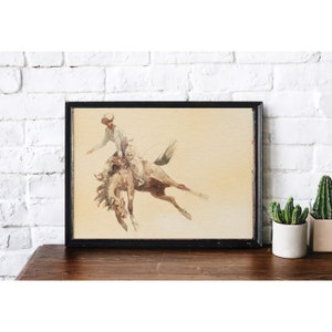 Puede incluir: Una pintura de acuarela vintage de un vaquero montando un caballo que se resiste. El vaquero lleva un sombrero y una camisa de color claro. El caballo es marr&oacute;n y blanco y est&aacute; en el aire.