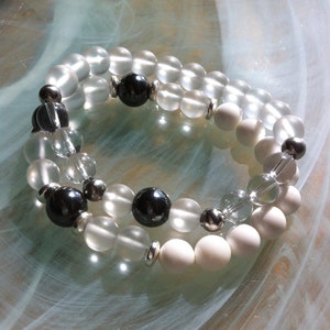 May include: A double-strand bracelet with white and black beads. The bracelet is made of frosted glass beads, black hematite beads, and silver spacers.