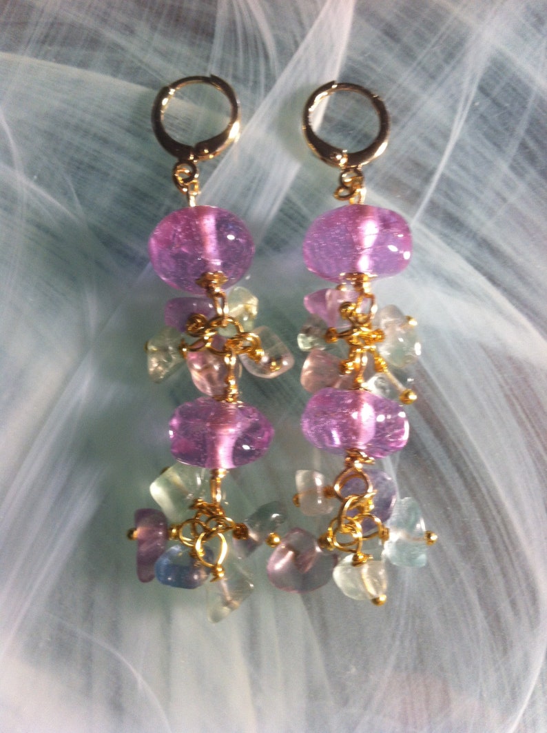 May include: A pair of dangle earrings with pink and green glass beads. The earrings have gold-toned hoops and are connected with gold-toned chains.