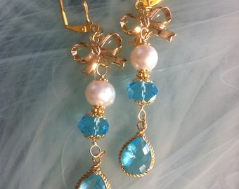 Earrings with faceted aqua-colored crystal rondelles and teardrops framed in gold plating and white freshwater pearls offered as a gift
