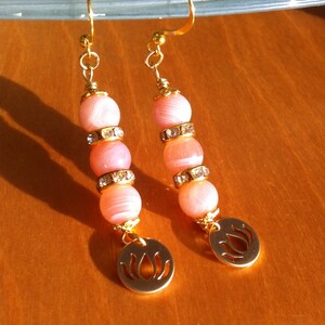 May include: A pair of gold earrings with pink and white beads and a gold lotus flower charm.