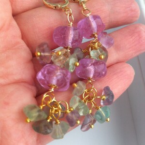 May include: Gold earrings with pink and green gemstone drops. The earrings feature multiple small gemstones hanging from larger pink gemstones.