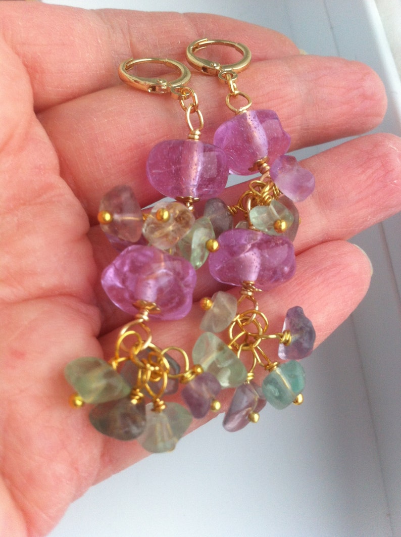 May include: Gold earrings with pink and green gemstone drops. The earrings feature multiple small gemstones hanging from larger pink gemstones.
