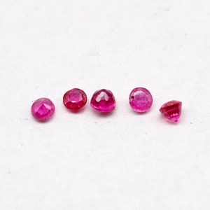 Può includere: Sei piccole pietre preziose di rubino rotonde e sfaccettate disposte in fila su una superficie bianca. Le pietre preziose sono di colore rosso intenso e hanno un'elevata lucentezza.