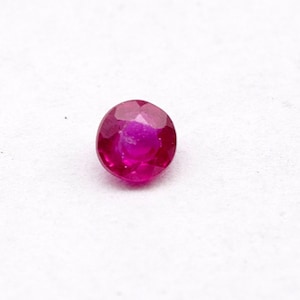 May include: A round, faceted, red gemstone. The gemstone is set against a white background.