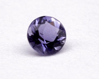 May include: A round, purple gemstone with a faceted cut. The gemstone is set against a white background.