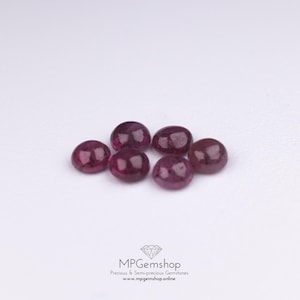 May include: Six oval, deep red gemstones are displayed on a white surface. The gems have a polished, smooth appearance, reflecting light. The image includes the text "MPGemshop Precious & Semi-precious Gemstones www.mpgemshop.online".
