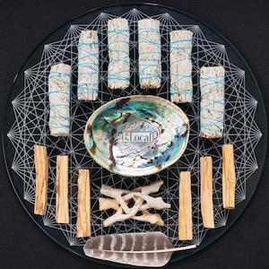 May include: A glass plate with a white geometric design, featuring a variety of smudging tools, including white sage bundles, palo santo sticks, a feather, and a seashell. The plate also includes the text "The Local".