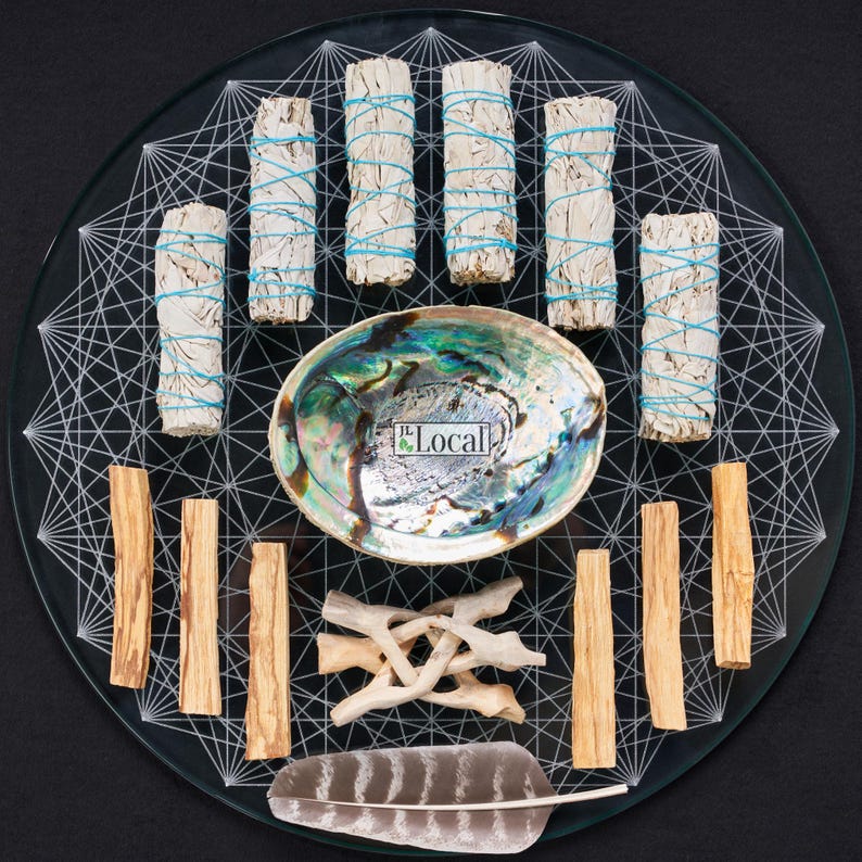 May include: A glass plate with a white geometric design, featuring a variety of smudging tools, including white sage bundles, palo santo sticks, a feather, and a seashell. The plate also includes the text "The Local".