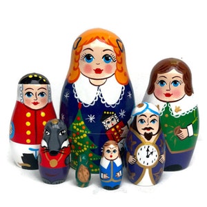 May include: A set of seven traditional Russian nesting dolls, or matryoshka dolls, depicting characters from the Nutcracker story. The largest doll is a girl with blonde hair wearing a blue dress with a white collar. The other dolls include a soldier, a mouse, a nutcracker, a girl in a blue dress, a man with a clock, and a girl with brown hair wearing a green dress.