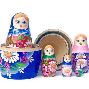 May include: A set of five traditional Russian nesting dolls, or matryoshka dolls. The largest doll is blue with white and pink floral designs. The other dolls are smaller and feature different floral patterns and colors, including red, green, and purple.