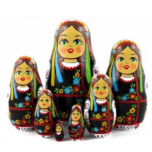 Può includere: Un set di sette bambole russe tradizionali, o bambole matrioska. Le bambole sono dipinte in uno stile di arte popolare colorato con motivi floreali e accenti neri, rossi, gialli, blu e verdi. La bambola più grande indossa un vestito nero con un motivo floreale e una fascia rossa. Le bambole sono disposte in ordine di grandezza, con la bambola più grande dietro e la bambola più piccola davanti.