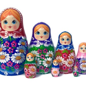 May include: A set of six traditional Russian nesting dolls, or matryoshka dolls. The dolls are painted with colorful floral patterns and feature smiling faces. The largest doll is blue with white flowers, the second largest is green with white flowers, the third largest is red with white flowers, the fourth largest is pink with white flowers, and the two smallest dolls are green and red with yellow flowers.