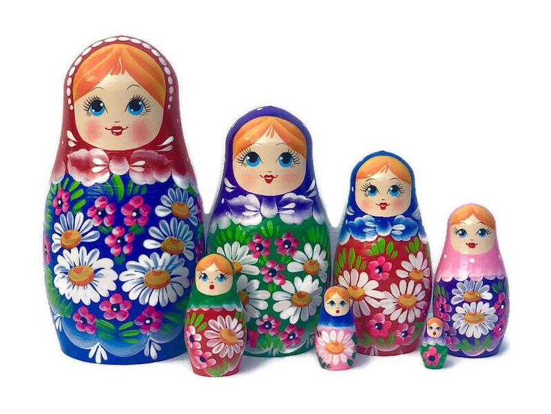 May include: A set of six traditional Russian nesting dolls, or matryoshka dolls. The dolls are painted with colorful floral patterns and feature smiling faces. The largest doll is blue with white flowers, the second largest is green with white flowers, the third largest is red with white flowers, the fourth largest is pink with white flowers, and the two smallest dolls are green and red with yellow flowers.