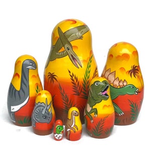 May include: A set of six yellow, orange, and green painted wooden nesting dolls, each featuring a different dinosaur. The largest doll depicts a pterodactyl flying over a jungle scene. The other dolls feature a stegosaurus, a triceratops, a brachiosaurus, and a smaller pterodactyl.