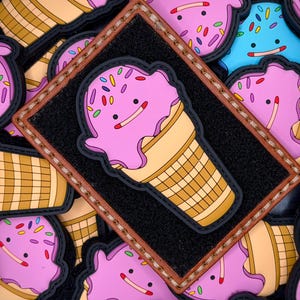 May include: A rectangular black patch with a brown stitched border featuring a rubberized ice cream cone character with pink ice cream, a tan waffle cone, and colorful sprinkles. The character has a simple face with two black eyes and a line mouth.