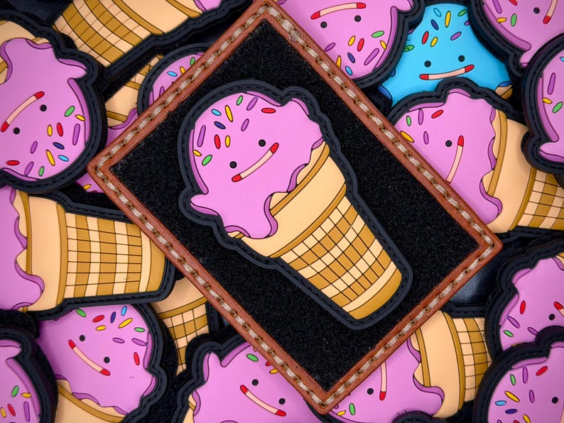 May include: A rectangular black patch with a brown stitched border featuring a rubberised ice cream cone character with pink ice cream, a tan waffle cone, and colourful sprinkles. The character has a simple face with two black eyes and a line mouth.