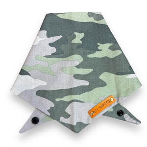 Puede incluir: Bandana para perros con estampado de camuflaje en tonos verdes, grises y blancos. La bandana es triangular y tiene un cierre de bot&oacute;n a presi&oacute;n. Una peque&ntilde;a etiqueta de cuero naranja con el texto "RUFF HIPPIE" est&aacute; adjunta.
