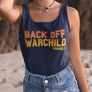 Può includere: Un top a spalline blu navy con la scritta "Back Off Warchild Seriously" in lettere gialle e arancioni. La modella indossa il top con pantaloncini di jeans e si trova su una spiaggia sabbiosa.